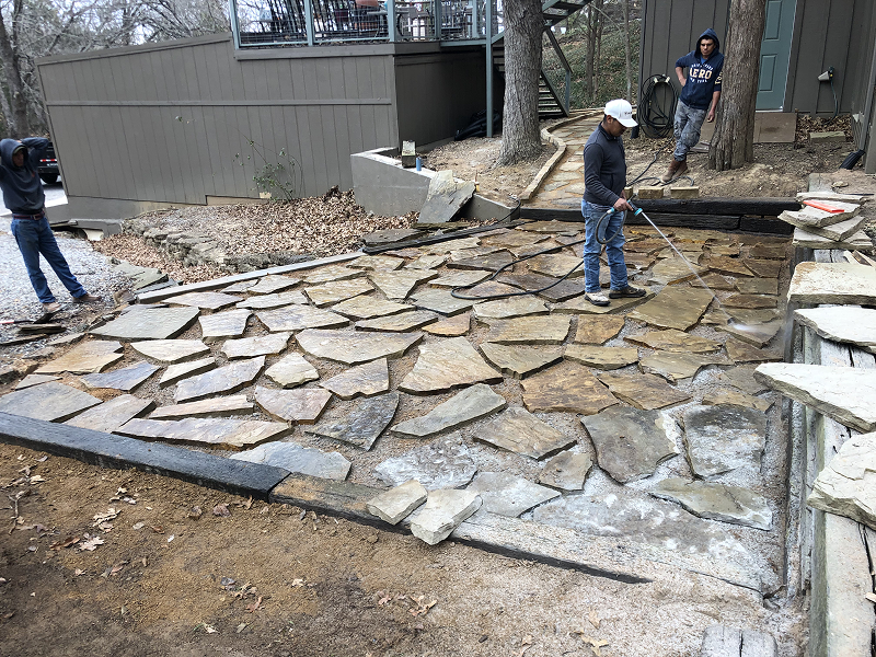 Three men working on installing a stone patio with irregular flagstones in a backyard near a house.