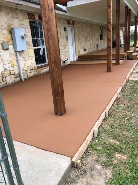 Newly poured brown concrete porch with wooden posts attached to a stone house exterior.