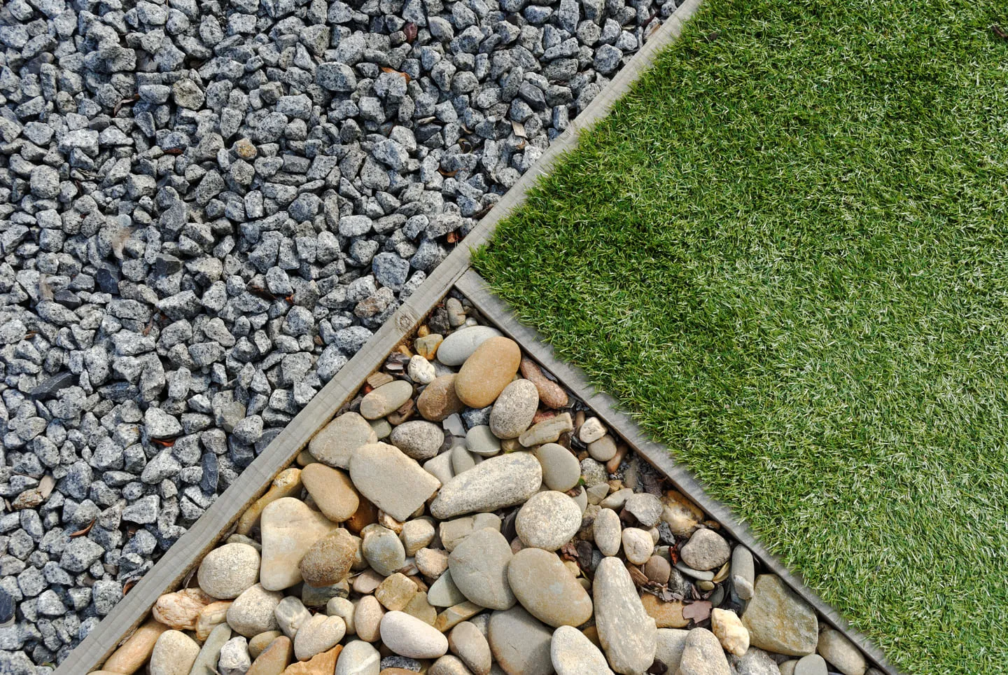 Overhead view of three square sections divided by wooden frames containing artificial grass, smooth river rocks, and coarse gray gravel.