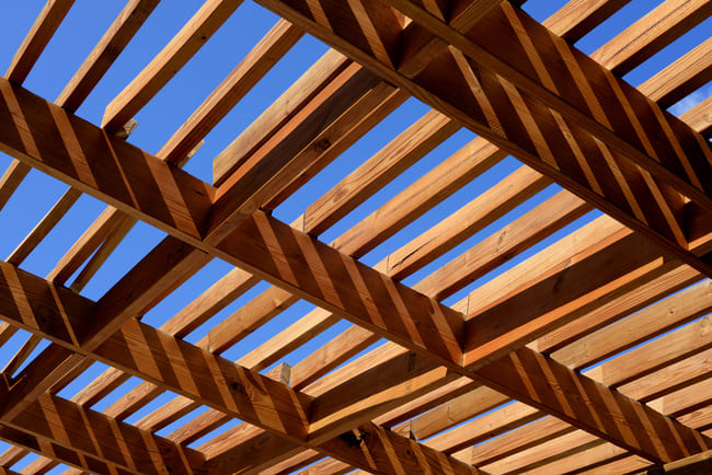 Wooden beams forming a lattice roof structure with bright blue sky in the background.