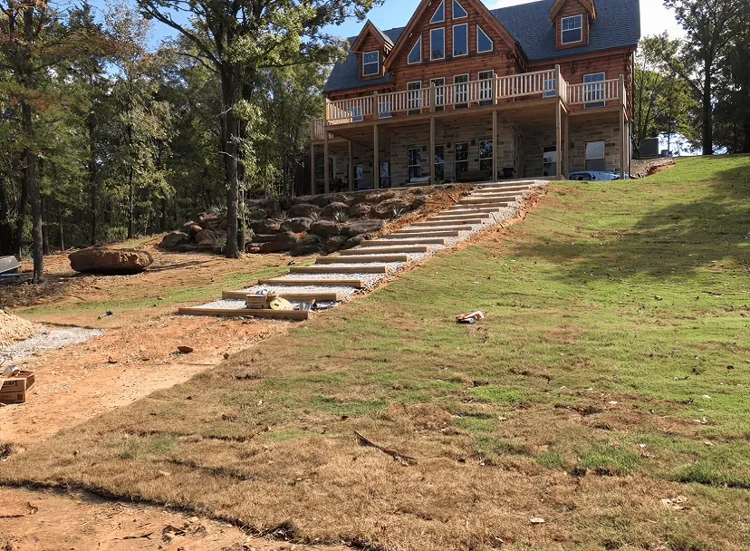 Large wooden house on a hill with new stone steps leading down through a grassy yard under construction.